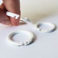 A hand demonstrates how to open and close white Plastic Snap Lock Binding Rings, with additional rings resting on a white surface.