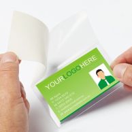 Hands sealing a green business card inside a clear 3-3/8" x 2-1/8" Wallet Size Gloss Self-Laminating Pouch with a peel-and-stick backing.