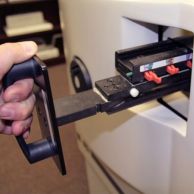 A person pulls out a die from a punch machine using a black handle, showing the modular design of the Dies for James Burn DocuPunch PLUS with clearly labeled disengageable pins for custom hole configurations.