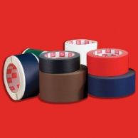 A selection of colorful adhesive tapes, including a roll of red fabric book repair tape positioned beside rolls of black, brown, blue, green, and white tape.