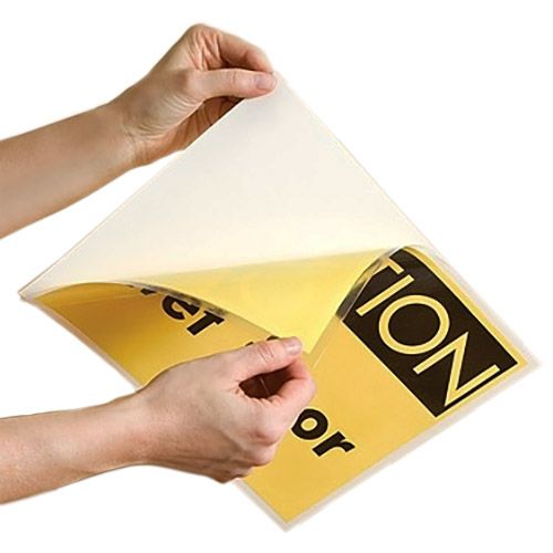 A person peels apart a sealed sheet containing a yellow sign inside 9" x 11 ½" Letter Adhesive-Back Laminating Pouches, revealing the clear protective layer over the adhesive backing.