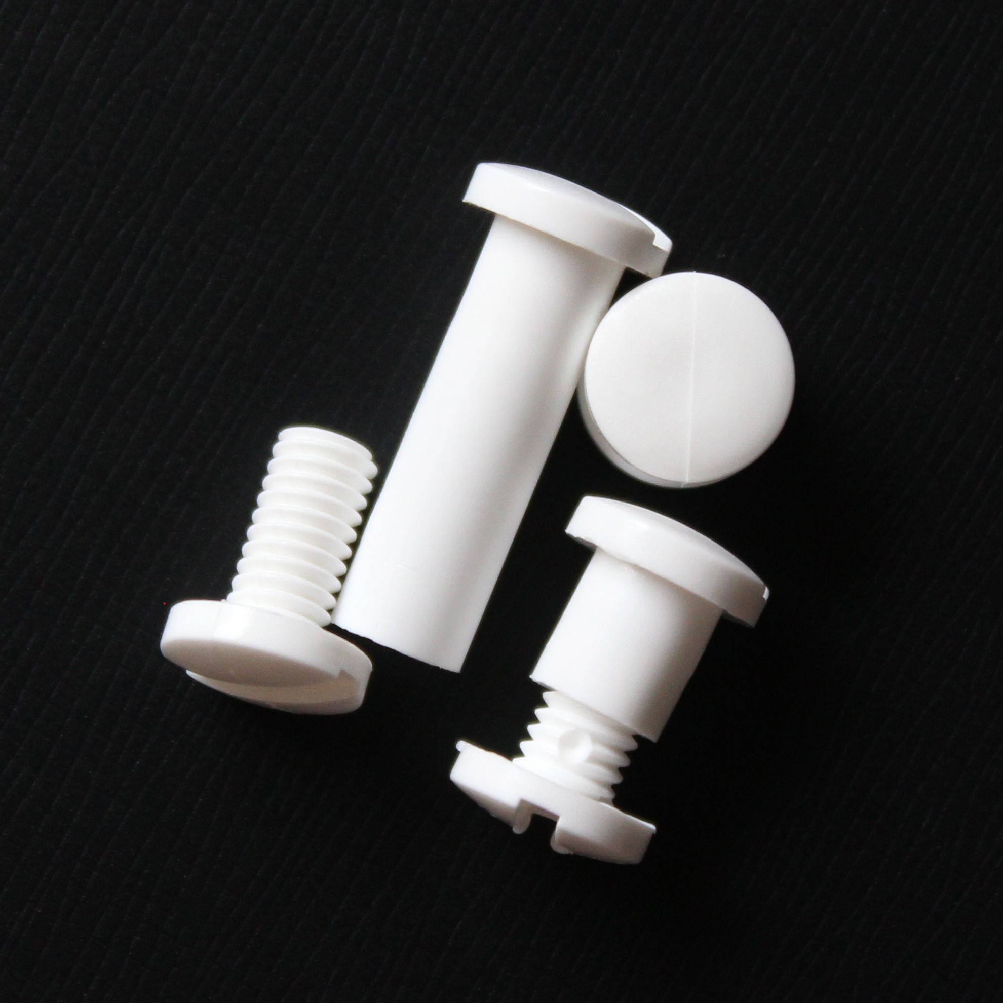 White Plastic Snap Lock Screw Posts displayed in various positions on a black textured surface, showing the interlocking threaded design and flat round heads used for binding loose materials securely.