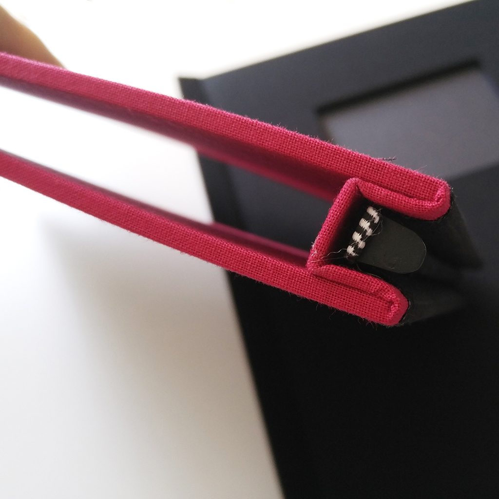Close-up view of the spine of Red and Black Pinchbook photo books, showcasing the vibrant red binding and sturdy construction.