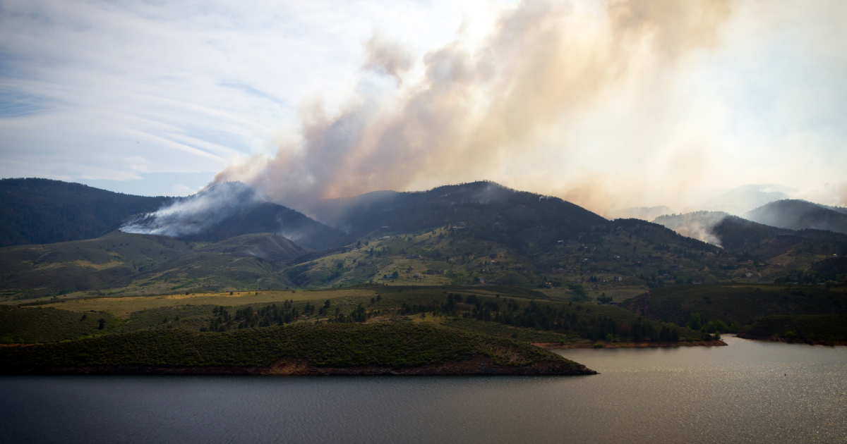 A panoramic view of a mountain range with wildfire smoke covering the clouds