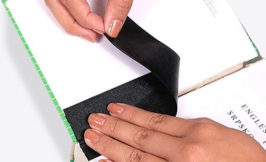 A person is applying black adhesive tape to the spine of a book for book care and repair.