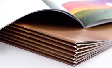 A stack of saddle stitch bound booklets, with a close-up view of their neatly stapled spines.