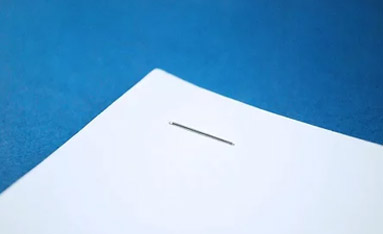 A close-up view of a single staple used for stapled documents binding on a sheet of white paper against a blue background.