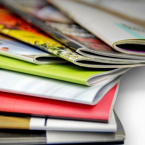 A close-up view of a stack of colorful saddle stitched magazines with pages slightly fanned out.