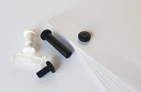 Plastic screw posts in black, white, and clear colors beside a stack of paper.