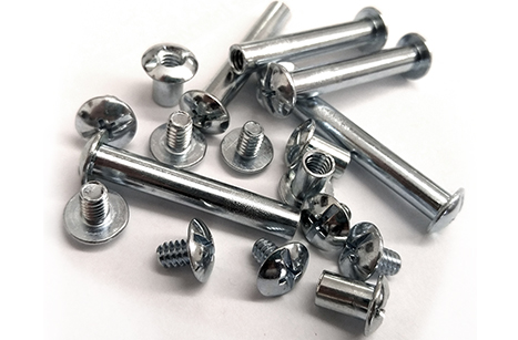 A collection of shiny steel screw posts in various sizes scattered on a white surface.